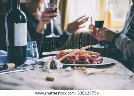 Restaurant or bar table with plate of appetizers and wine. Two people talking on background. Toned picture