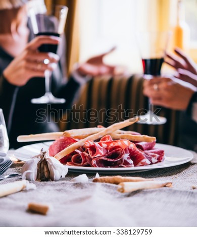 Restaurant or bar table with plate of appetizers and wine. Two people talking on background