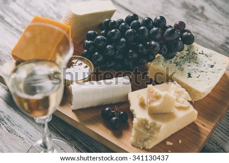 Different types of cheese with grape on wooden board served with the glass of white wine. Toned image