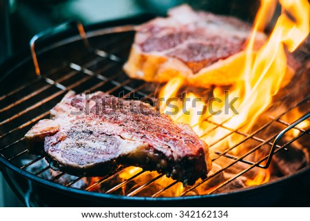 Two t-bone florentine beef steaks on the grill with flames