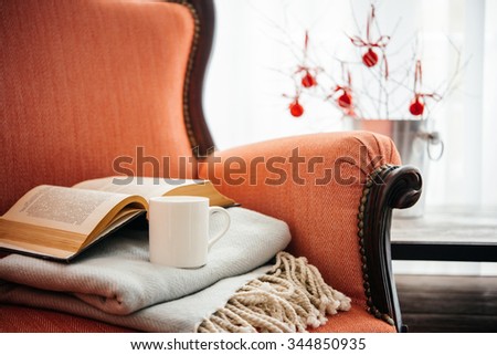 Book, cup and warm plaid on cozy retro armchair. Christmas or new year decoration concept