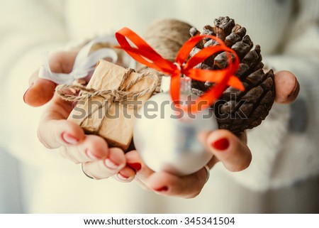 Woman\'s hands hold christmas or new year decoration. Small gift box, glass ball and cone. Toned picture