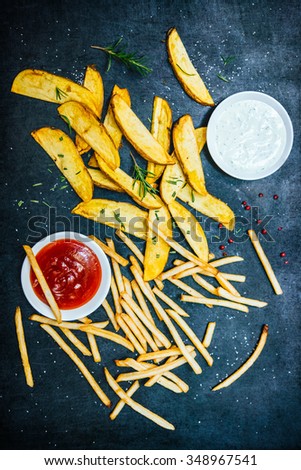 French fries and fried potato wedges with herbs and sauces on black background