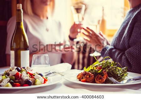 Restaurant or cafe table with plate of salads and wine. Two people talking on background. Toned picture