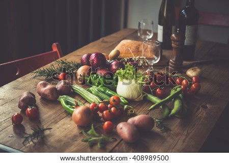 Different fresh farm vegetables on wooden table. Wine bottles and bread on background. Autumn harvest and healthy organic food concept. Toned picture