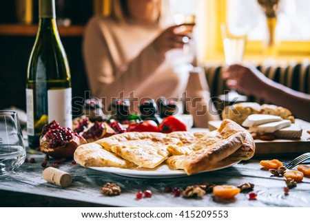 People are having traditional georgian lunch or dinner of khachapuri, aubergine rolls, imeretian and suluguni cheeses and wine served on wooden table.
