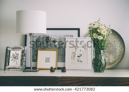 Framed pictures, flowers and lamp on wooden console. Living room interior and home decor concept. Toned picture