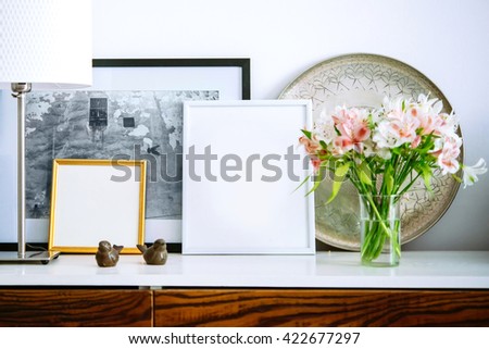 Living room decoration. Framed pictures, flowers and lamp on wooden console