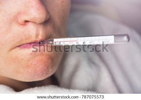 Sick woman with seasonal flu measuring body temperature with thermometer in her mouth reaching 38 degrees celsius