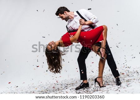 It is hot salsa! Full length of young beautiful couple dancing while standing against white background with confetti