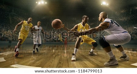 Basketball players on big professional arena during the game. Tense moment of the game. Male caucasian and black players fight for the ball