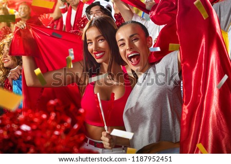 Young sport supporter happy fans cheering at stadium. Beautiful girls with flags support the football team during the match