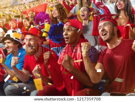 Young sport supporter happy fans cheering at stadium. Group of young woman and man support the football team during the match