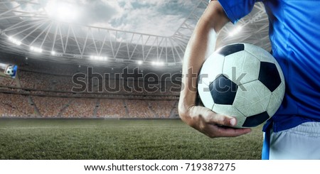 Soccer player holds a soccer ball on a professional stadium. Player wears unbranded clothes.