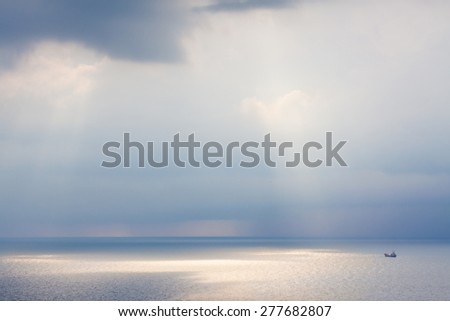 Ship in a sea. Sun rays from clouds. Rain in open sea