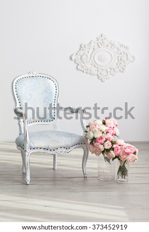 Elegant light-blue arm-chair and tender flowers near white wall. Interior in white colors
