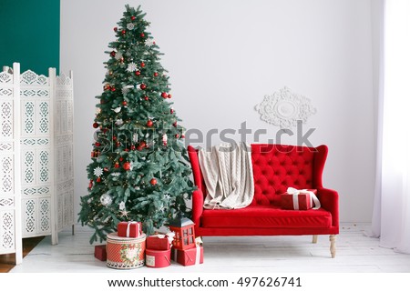 Stylish Christmas interior with an elegant red sofa. Comfort home. Armchair with fabric upholstery. Christmas tree with presents underneath in living room