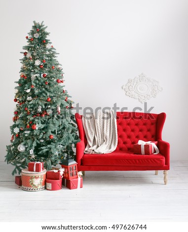 Stylish Christmas interior with an elegant red sofa. Comfort home. Armchair with fabric upholstery. Christmas tree with presents underneath in living room