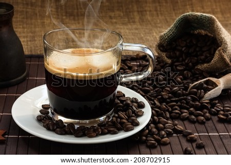 A glass of steaming hot fresh coffee on a white plate with coffee beans