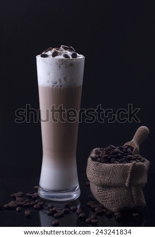 A glass of tasty italian latte macchiato with a bag of coffee beans on a plain black background and black reflection
