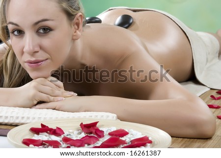 Smiling female face - Hot stone massage in the day spa - Portrait of a beautiful young girl at the day spa with black stones on her bare back