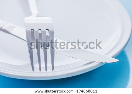 plate with crossed silver knife and fork cutlery, shallow deep of field with focus on tip of fork