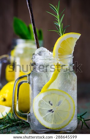 Lemonade with fresh lemon and rosemary in glass on wooden background