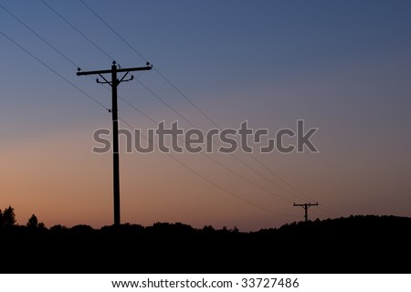 A silhouette of electric power lines flow across a colorful dusk sky.