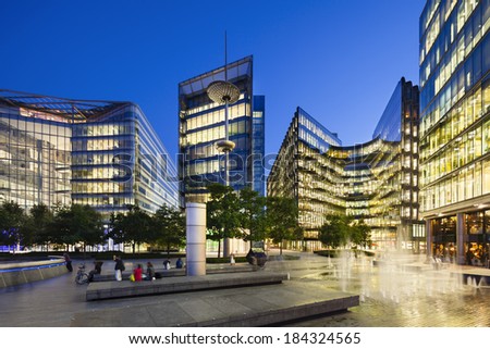 Night view of several modern glass buildings near City Hall in London with blue night sky and some fountains