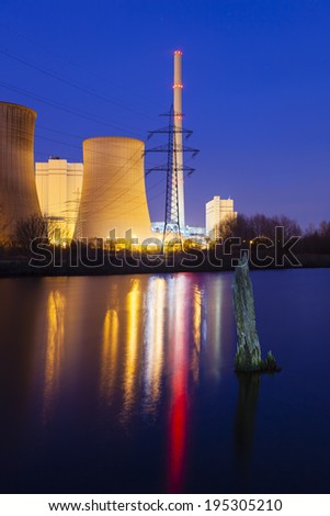 A coal-fired power station in river landscape with dead tree at night