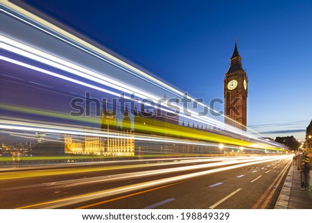 Long exposure night shot of the Houses of Parliament in London with blue sky and a bus passing on Westminster Bridge in the foreground.