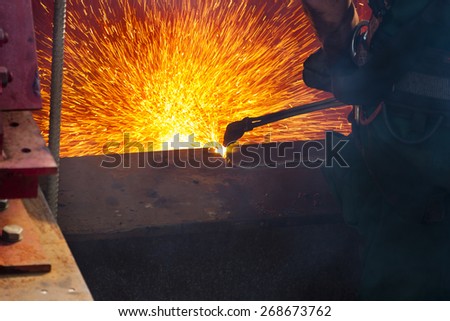 Worker cutting a steel beam of an old bridge with sparks flying around.