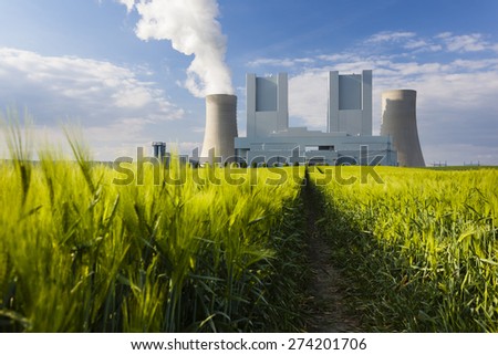 Low angle view of a shiny new lignite power station behind a rye field with wheel tracks leading to it. Focus on the power station.