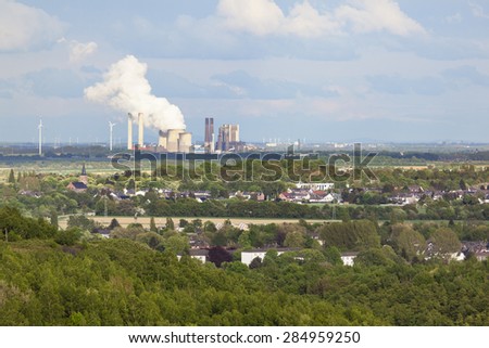 View from a slag heap over rural landscape to a distant steaming coal-fired power station.