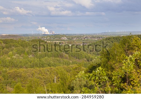 View from a slag heap over green forest in west Germany near Aachen to a distant coal-fired power station.