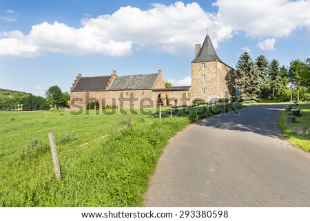 A country road leading to old farm buildings fortified like a small castle in the North Eifel, Germany