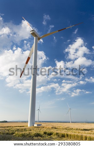 A close wind turbine in a wind park that seems to look down at smaller wind turbines in the background. Seen in the Eifel, Germany.