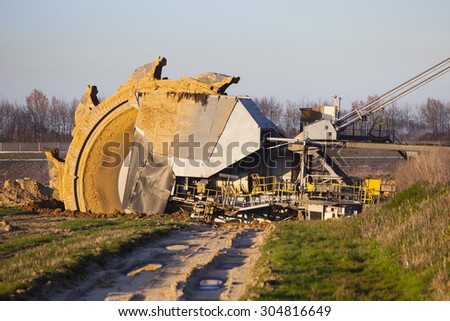 A giant Bucket Wheel Excavator at work in a lignite pit mine with a dirt road leading to it in the foreground