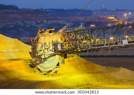 A giant Bucket Wheel Excavator in a lignite pit mine at night. The sign says \'Approaching the machine during work is prohibited\' in German.