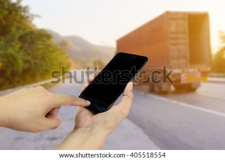 Hand holding and touch screen smart phone,cellphone on roadside with Trucks transporting in background Asian