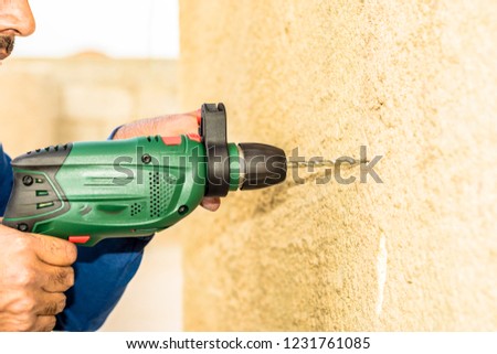 a professional mason is making whole into concrete wall by his drill machine