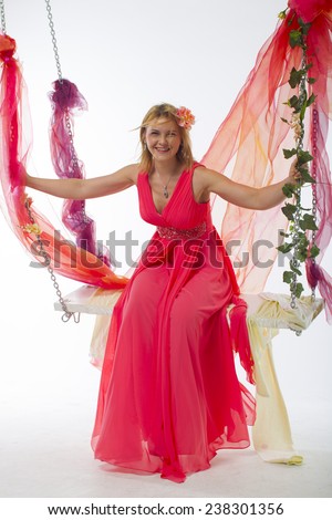 beautiful young woman on a swing in a bright pink (salmon color) long dress with flowers in her hair sitting on a swing on a white background, right