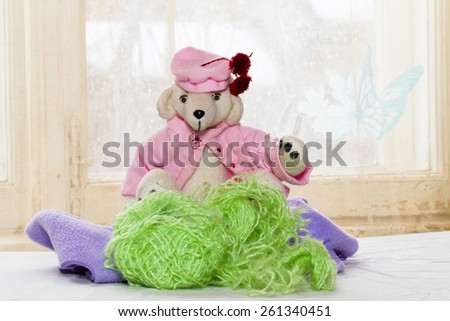 teddy bear in pink blouse and pink beret with red pom-poms on the background of bright windows, a bright sunny day and a festive spring mood. Tangles and threads,