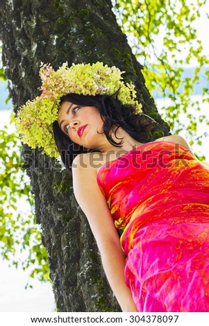 young Russian woman on her head a wreath of flowers hydrangeas, a woman relaxed, reclining on a tree trunk, happy, Russian traditions and folk life and the way of clothing, intimate nature.