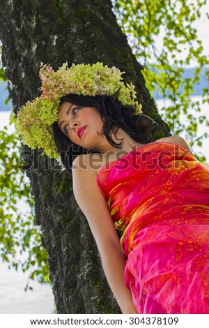 young Russian woman on her head a wreath of flowers hydrangeas, a woman relaxed, reclining on a tree trunk, happy, Russian traditions and folk life and the way of clothing, intimate nature.