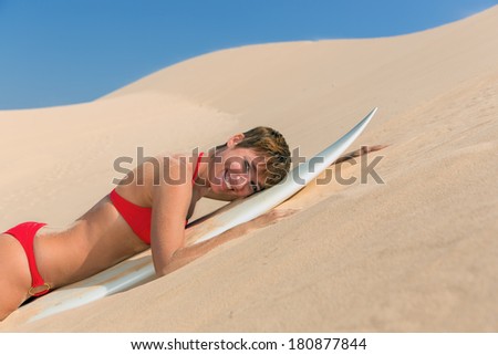 Rear view of beautiful sexy young woman surfer girl in bikini with white surfboard on a beach in desert