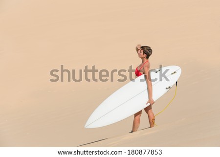 Rear view of beautiful sexy young woman surfer girl in bikini with white surfboard on a beach in desert