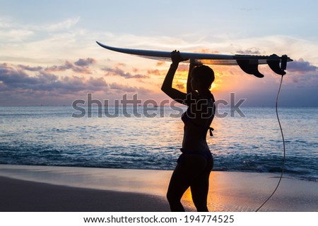 woman surfer with surfboard on tropical beach at sunset