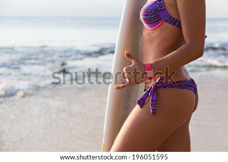 Rear view of beautiful sexy young woman surfer girl in bikini with white surfboard on a beach at sunset or sunrise