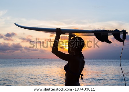 woman surfer with surfboard on tropical beach at sunset